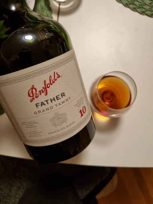 Flaska av "Penfolds Father Grand Tawny" vid sidan av ett glas med bärnstensfärgad dryck.