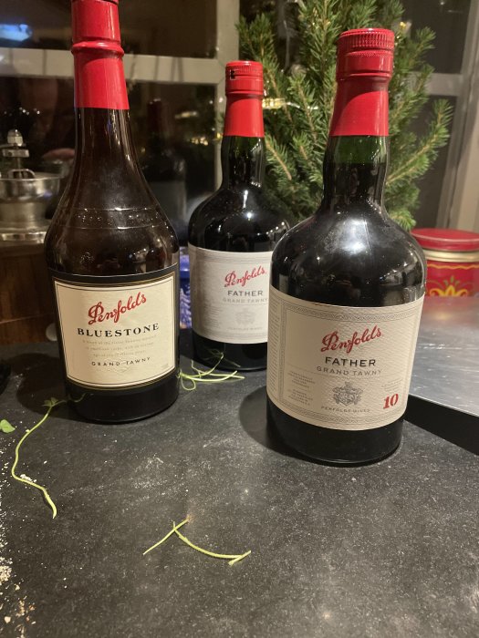 Tre Penfolds vinflaskor, "Grand Tawny", på ett köksbänk, med en julgran i bakgrunden.