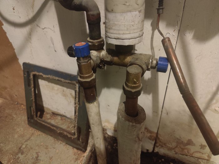 Rörsystem med ventiler, anslutningar och isolering mot smutsig vägg i källare.