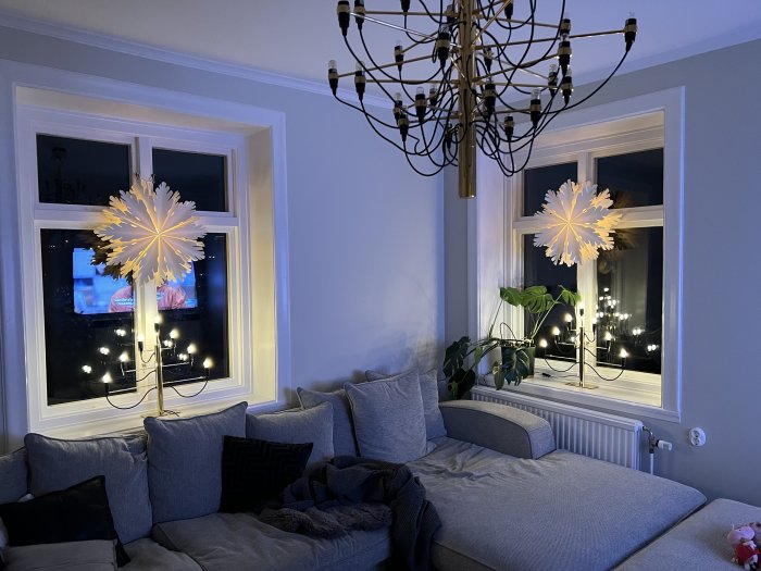 Ett mysigt vardagsrum med soffa, stjärnlampor i fönstren och en takkrona.