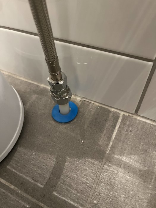 Vittoledning vid toalett, blå tätningsskiva på grått kaklat golv.