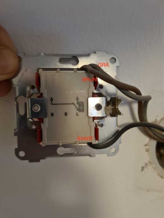 Öppen elektrisk väggströmställare med exponerade kablar märkta i färger: grå, brun, svart.