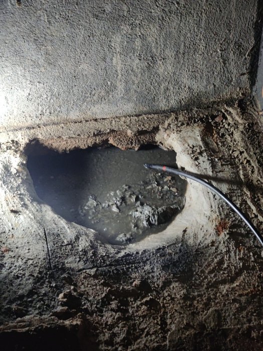 Vattenläcka, hål, betong, korrosion, mörker, rörledning, skadad infrastruktur, behov av reparation.