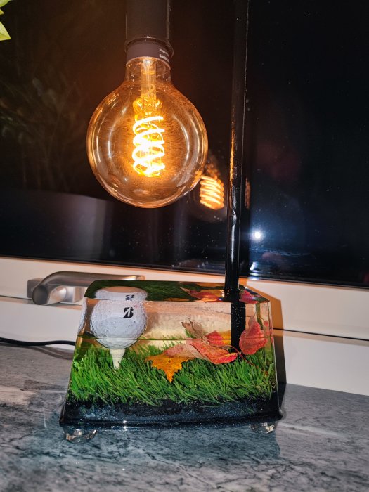 Glödlampa med synlig filament, spegelreflexion, dekorerad svart lampfot med golfmotiv.