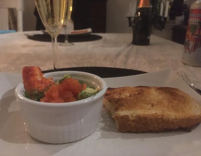 En rostad skiva bröd, skål med röra och kaviar, champagne, mysig miljö, middagsstämning.