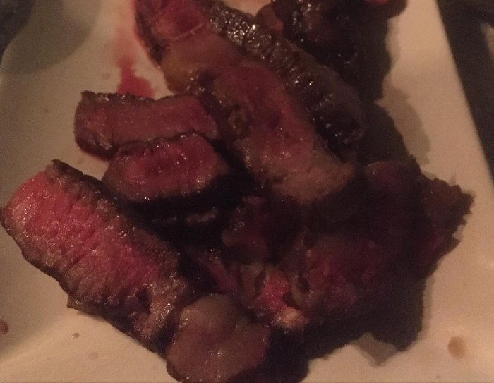 En tallrik med skivad, stekt eller grillad köttbit, ser saftig ut, mörk belysning, middagsmiljö.