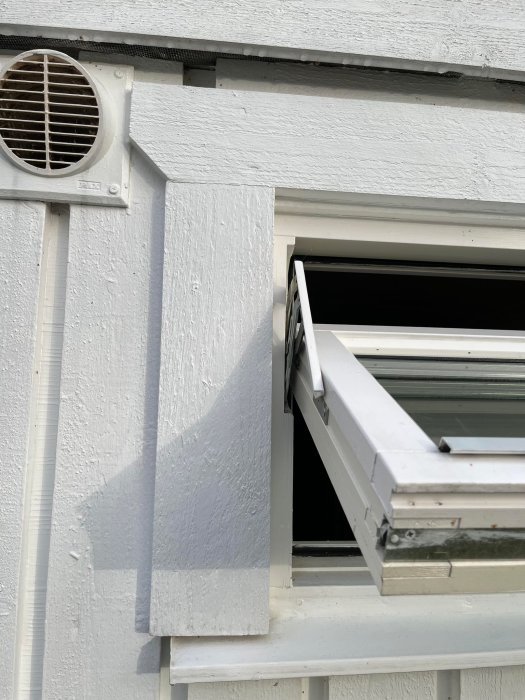 Vit vägg med öppet fönster, ventilation, skugga, träpanel, dagtid.