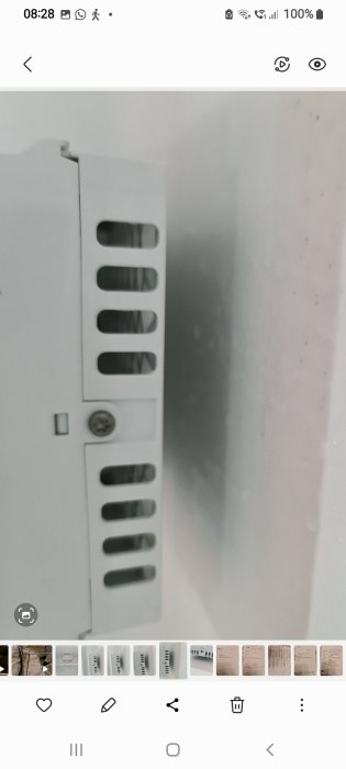Vit vägg med en elcentral och skuggor, mobilskärm med ikoner och tid överst.