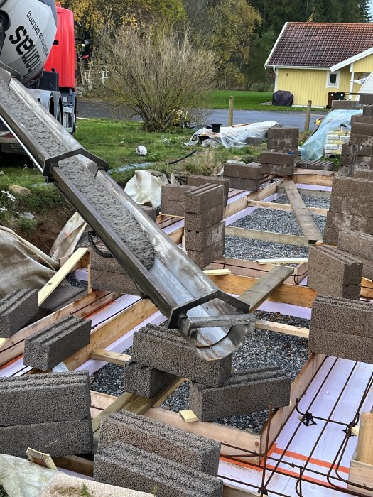 Byggarbetsplats med lastbil, färsk betong, armering och betongblock i dagsljus.