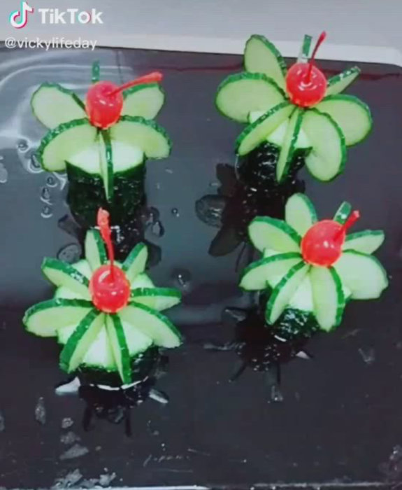 Gurkdekor i form av blommor med körsbär på toppen, presenterade på en reflekterande yta.