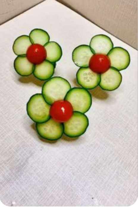 Två blommor gjorda av gurkskivor och körsbärstomater på en ljus bakgrund.