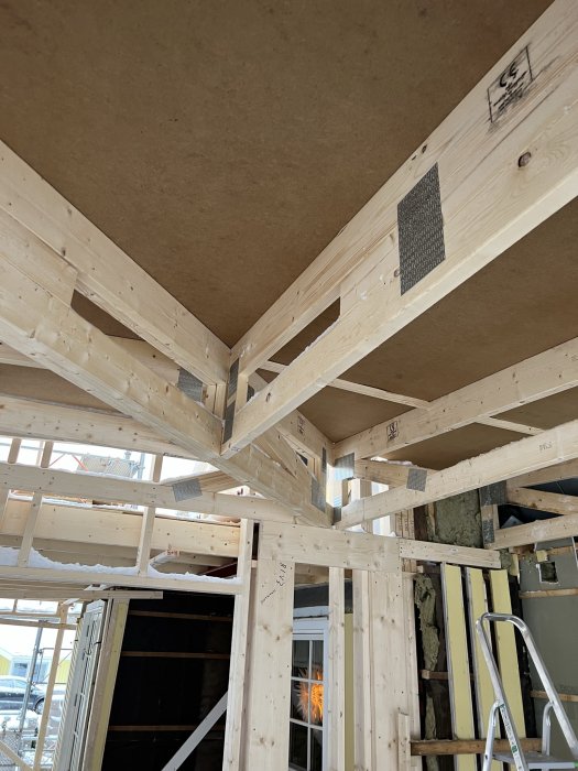 Träkonstruktion för byggnadsstomme under uppbyggnad, synliga balkar, isolering och takskivor. Inomhusbild från en byggarbetsplats.