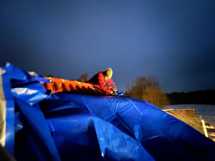 En person sitter på toppen av ett blått uppblåsbart föremål på kvällen utomhus.