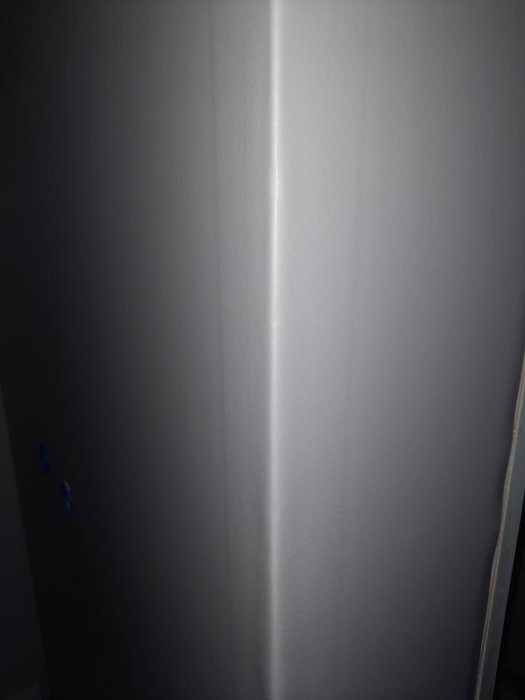 Ljus på en vit vägg med hörn, mörk del till höger, suddiga blå prickar till vänster.