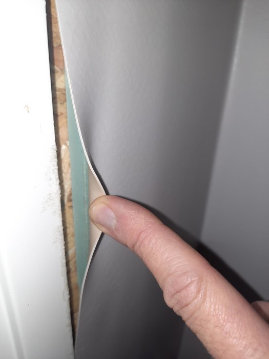 En person pekar på en lucka mellan vägg och vit panel. Närbild, byggdetalj, hemförbättring, ojämn anslutning.