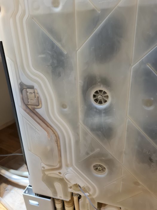 Inuti en tvättmaskin sedd från undersidan med sladdar och mekaniska komponenter synliga.
