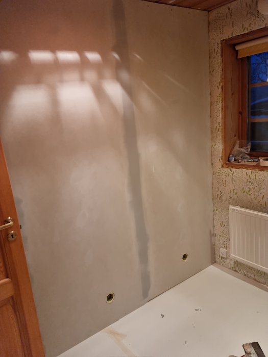 Renoveringsrum, vägg utan kakel, två avloppshål, fönster, dörr, tapet, skuggor, radiator, nattetid.