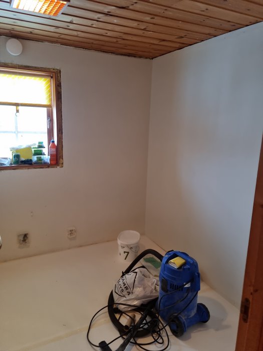 Tomrum, renovering, träbjälkar i taket, fönster med gult ljus, dammsugare och byggmaterial på golvet.