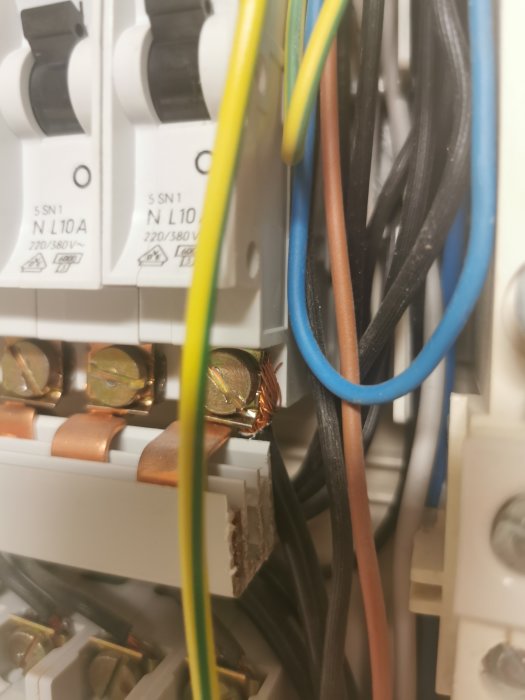 Elektriskt skåp med kablar och säkringar; skada på en kopparledare synlig. Säkerhetsrisk möjlig.