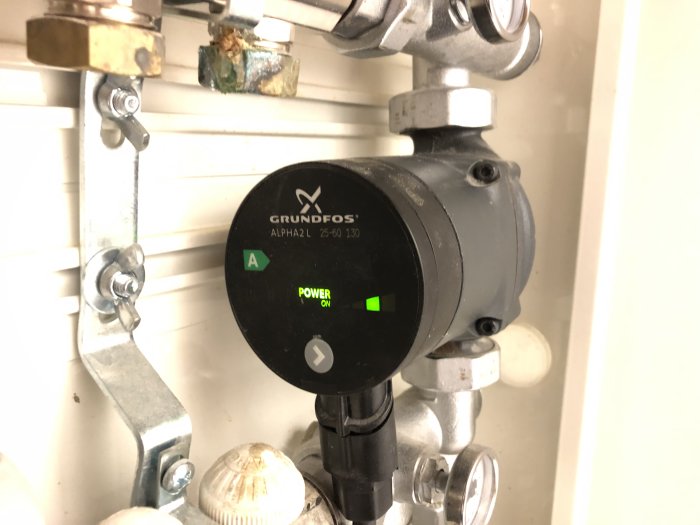 Grundfos cirkulationspump installerad på rörsystem, grön strömindikator lyser, pumpen är igång.