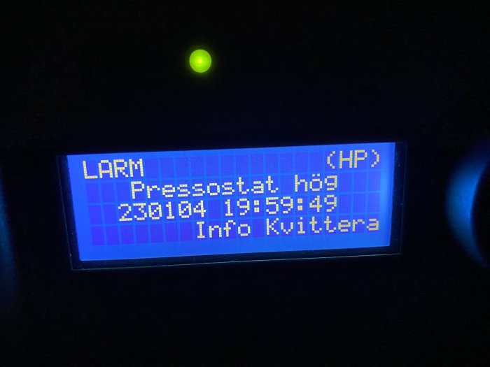 Digital skärm visar larm för högt tryck, datum-tid-stämpel, kräver åtgärd. Mörk bakgrund, grönt ljus ovanför.