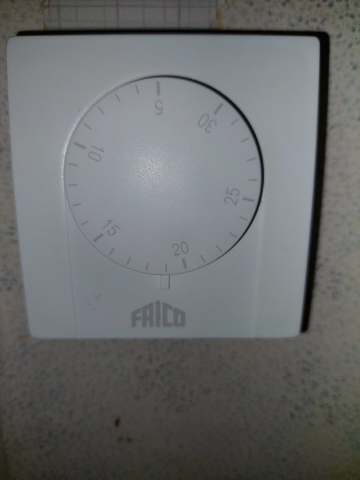 Väggmonterad termostat, vitt skal, reglertavla, varumärket Frico, gradmarkeringar, smutsfläckar, enkelt brukargränssnitt.