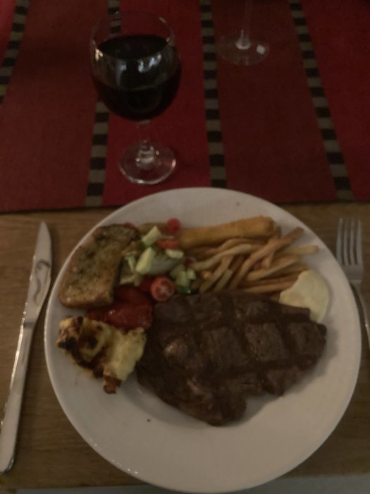 Middagsdukning med biff, pommes frites, sallad, vitlöksbröd och ett glas rött vin. Ambiance ser mysig ut.