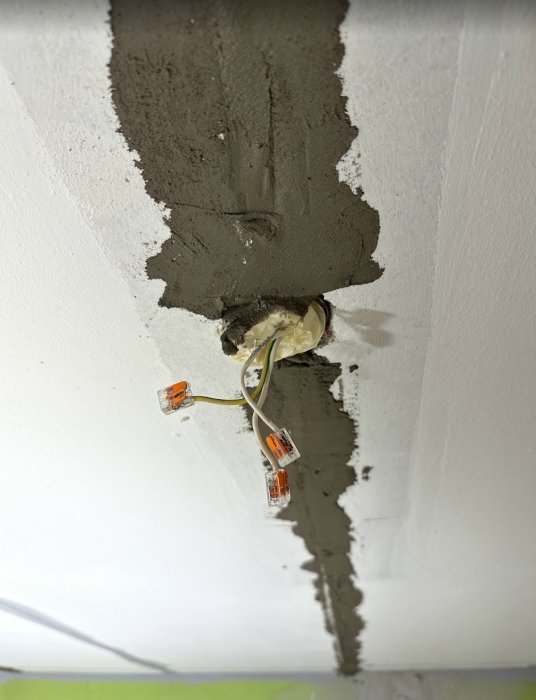Reparationsarbete på vägg, elinstallation med kablar och kopplingsklämmor, omålade putsområden, konstruktion under progress.