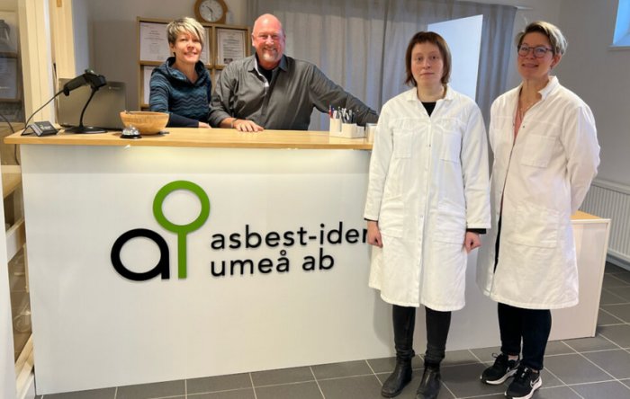 Fyra personer i en reception, två i vita rockar, logotyp, "asbest-idé umeå ab".