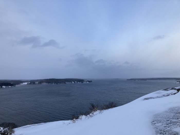 Vinterlandskap, snötäckt mark, grå himmel, lugnt hav, molnigt, skymning, ödsligt, kallt.