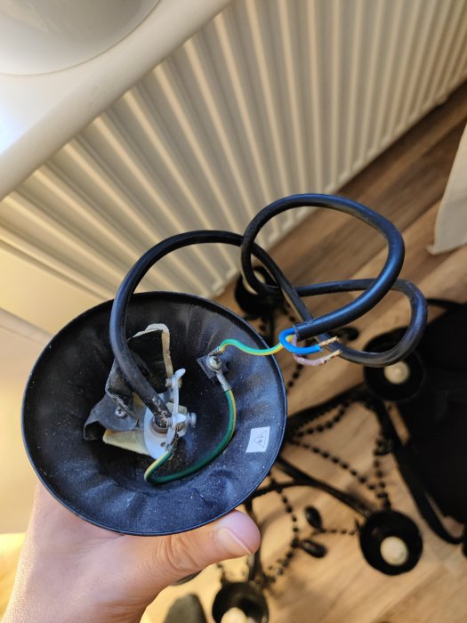 En hand håller en lampa med synlig elanslutning och ledningar mot en suddig bakgrund av ett rum.