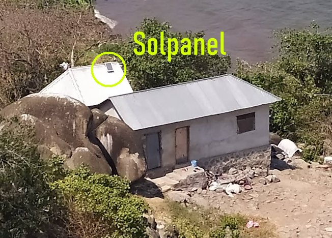 Hus vid vatten, solpanel på taket, stora stenar, markerat element, avskilt läge, skräp runtomkring.