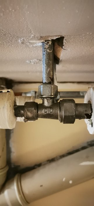 Vattenrör av metall med anslutningar och muttrar, under tak, nära andra rörinstallationer.
