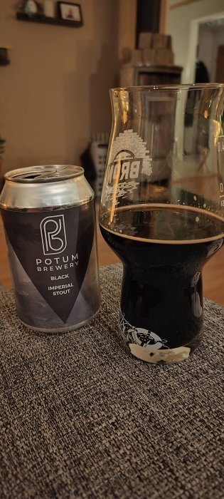 En burk och ett glas med mörkt öl, Potum Brewery Imperial Stout, inomhus på ett bord.