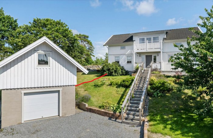 Vitt hus med balkong, garage, grön trädgård, stentrappa och klar himmel.