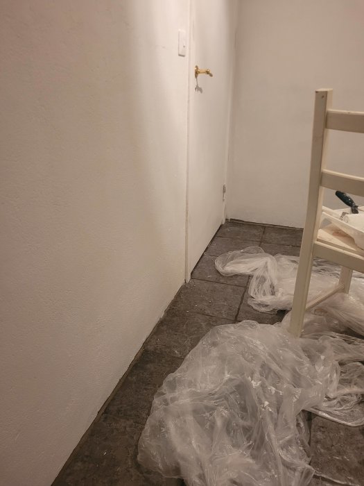 Vitmålad vägg, guldig kran, stolben, plast på golv, inomhus, renovering eller målararbete pågår.