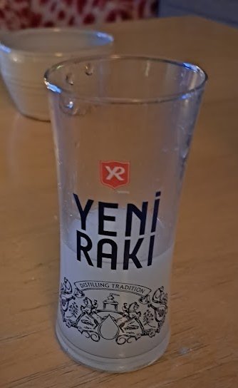 Ett tomt Yeni Raki-glas på bord, traditionella bilder, mätmarkeringar. Bakgrunden är suddig med koppar.