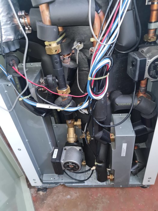 Inuti en värmepump med synliga rör, kablar, och komponenter, möjligen under underhåll eller reparation.