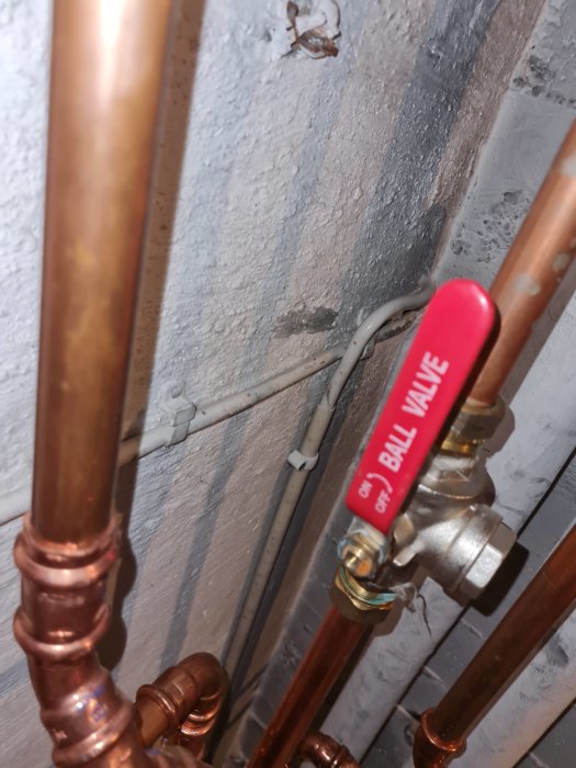 Kopparledningar, ventiler, grå vägg, elledningar, röd märkt kulventil för avstängning, installation inomhus.