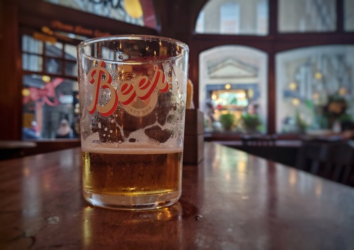 Ölglas halvfullt, bordsutsikt på pub, inredningsdetaljer suddiga i bakgrunden.