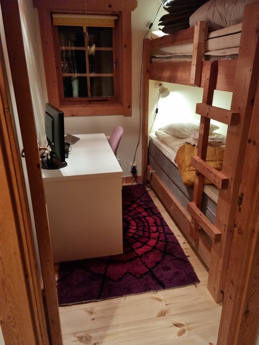 Kosigt sovrum med våningssäng, trädetaljer, skrivbord, rosa stol och röd matta.
