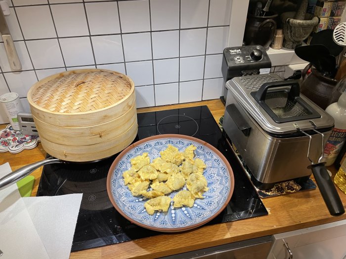 Kök med bambuångare, friterade varor på tallrik och fritös. Matlagning, köksutrustning, kakelvägg.