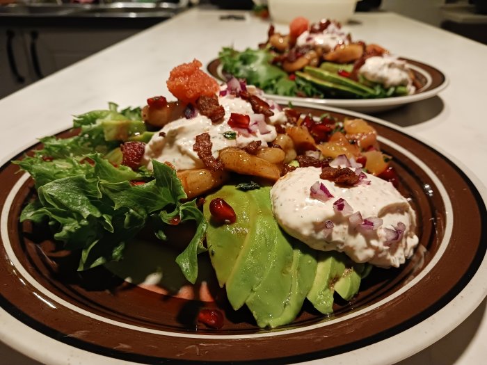 Färgrik maträtt med sallad, avokado, toppingar, krämig sås på en keramiktallrik.