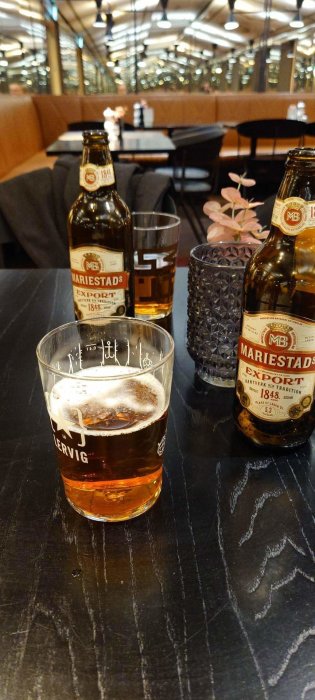Ölglas och flaskor på bord, Mariestads Export, inomhusmiljö med speglingar och sittdelar, belysning i taket.