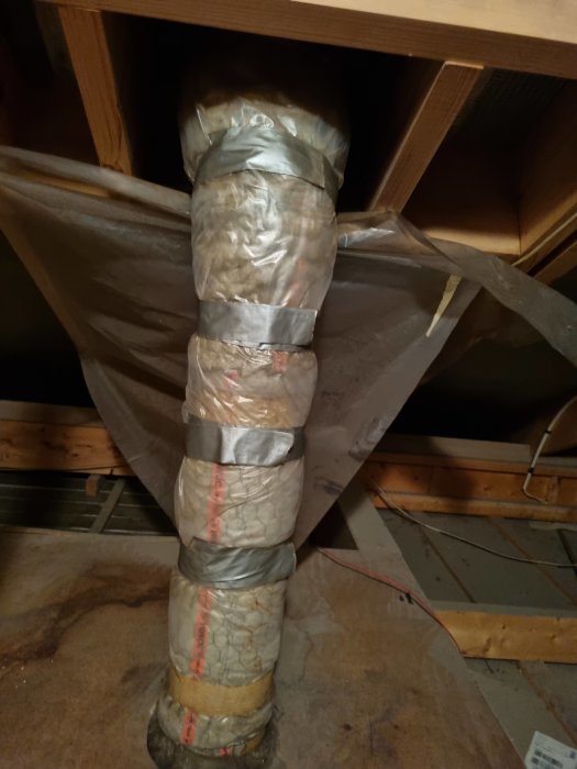 Isolelemente rör med tejp, plast, isoleringsmaterial i ett oisolerat loftutrymme, med synliga träbjälkar.