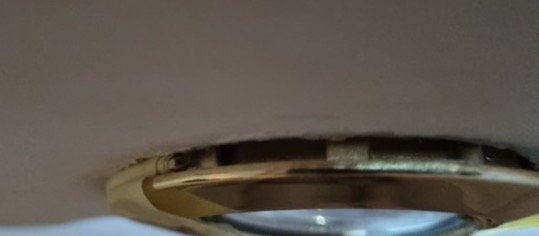 Närbild på en ring med reflektion, mot suddig bakgrund. Detaljer oklara, möjligtvis guldfärgad.