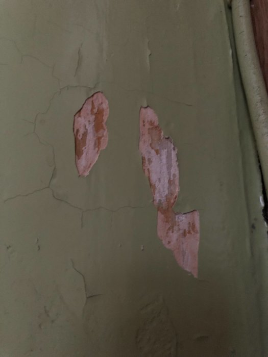 Föråldrad vägg med färg som flagar och sprickor, behöver renovering.