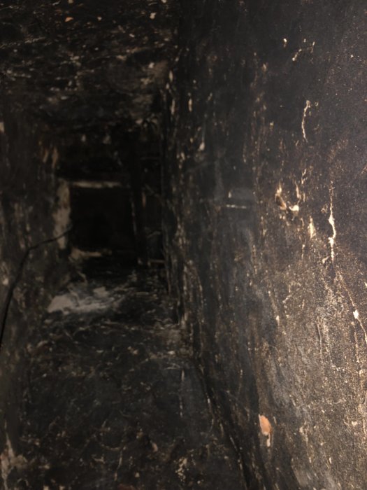 Mörk, smutsig ventilationsschakt eller gång med kabel, debrisspår, och slitage. Verkar övergiven eller i behov av underhåll.
