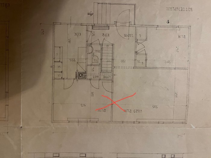 En uppochnervänd planritning av en bostad med ett rött kryss markerat på det.