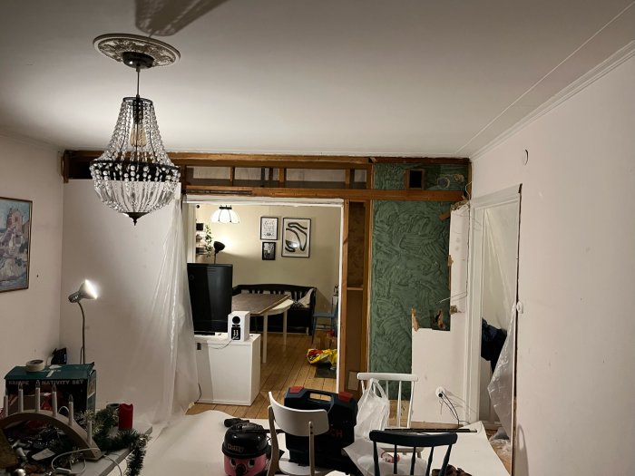 Ett rum under renovering med synliga träbjälkar, byggmaterial, belysning och inredningsdetaljer.